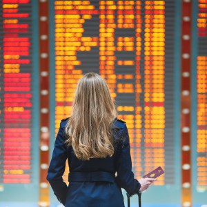 Young woman in international airport looking at the flight information board, checking her flight